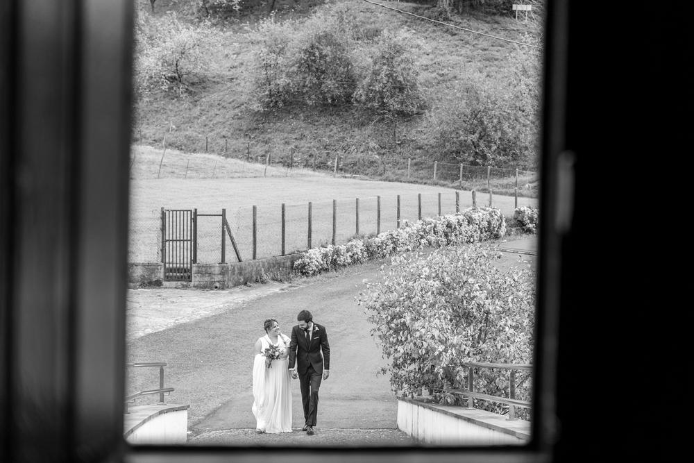 Novios paseando de la mano vistos a través de una ventana, en blanco y negro, boda en Hernani.