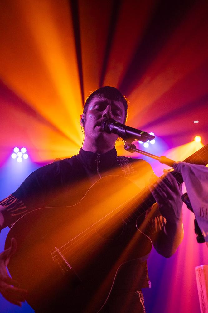 Cantante de Islakume con guitarra bajo luces naranjas y rosas en Dabadaba, San Sebastián.