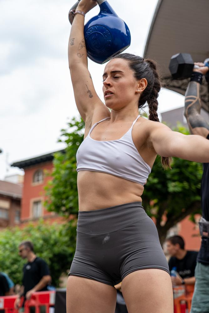 Deportista levantando una kettlebell azul sobre la cabeza en una competición de CrossFit en Erandio.